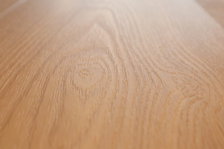 Close-up van een houten vloer met een lichte eiken uitstraling, waarbij de natuurlijke houtstructuur en nerven duidelijk zichtbaar zijn.