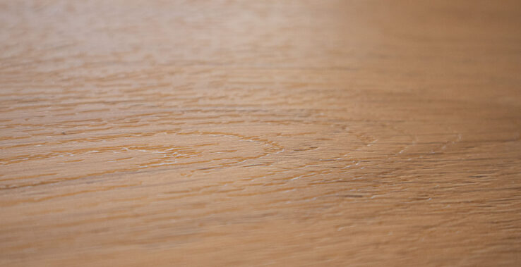 Close-up van een lichte houten vloer met subtiele nerfstructuren, die een warme, natuurlijke uitstraling geeft.
