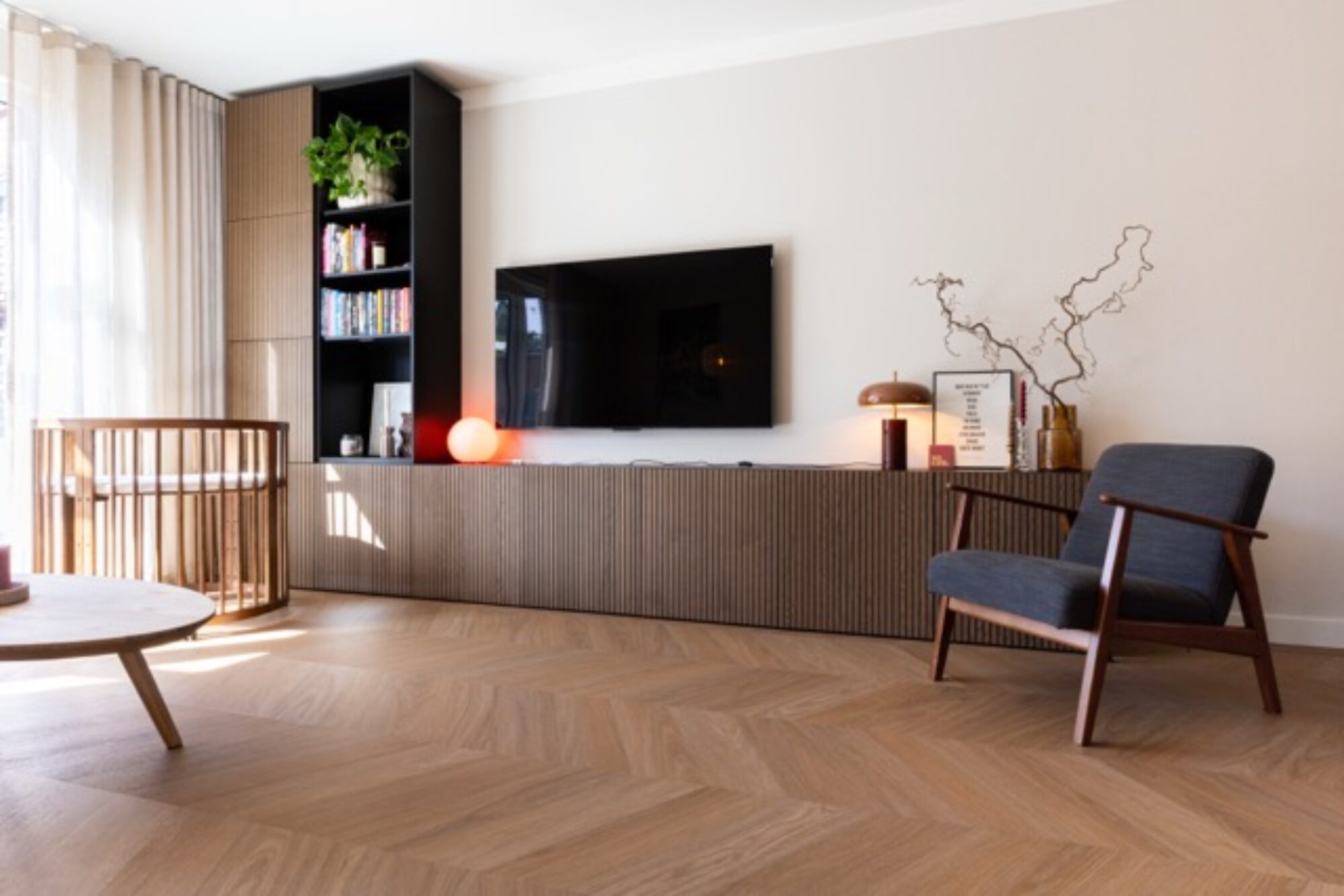 Woonkamer in Deventer met tv-meubel, boekenkast, fauteuil en houten visgraatvloer