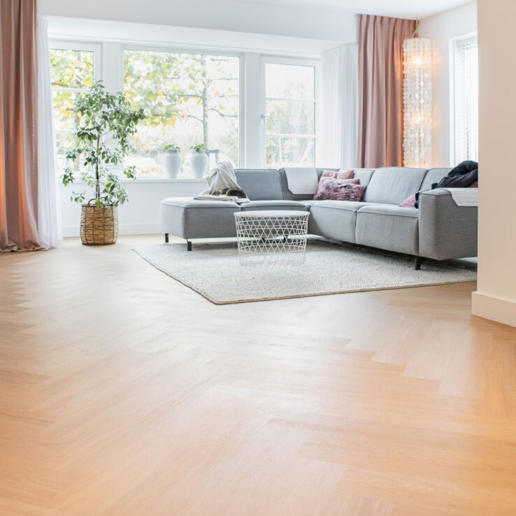 Lichte eiken PVC-vloer in een moderne woonkamer met een comfortabele bank, veel natuurlijk licht en een gezellige sfeer.