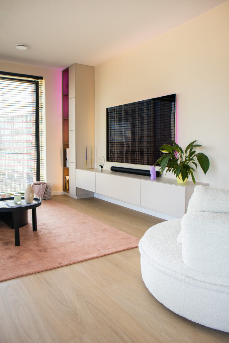 Lichte eiken PVC-vloer in een moderne woonkamer met tv-meubel, roze vloerkleed en ronde witte fauteuil.