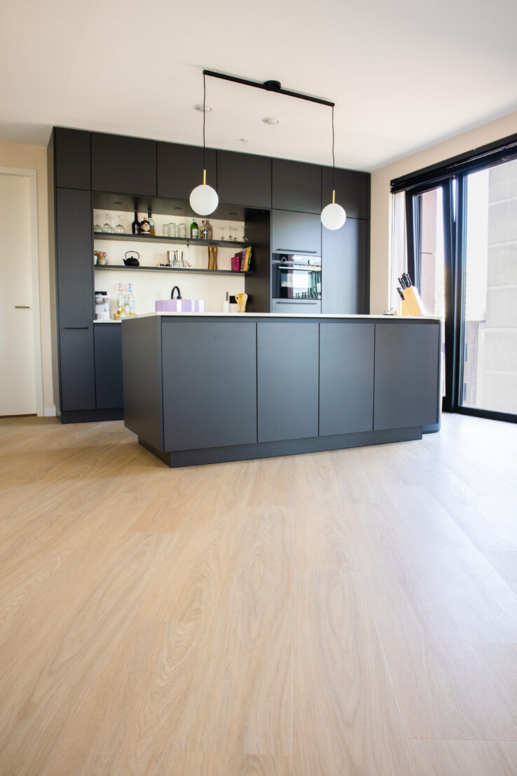 Moderne keuken met matzwarte kasten en kookeiland, gelegen op een lichte eiken PVC-vloer met brede planken.