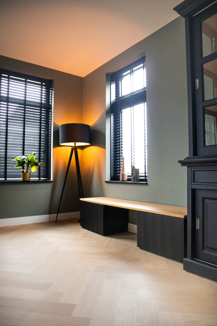 Lichte eiken visgraat PVC-vloer in een stijlvolle hoek met zwarte shutters, een staande lamp en een houten zitbank.