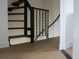 Open trap met houten treden en zwart metalen leuning, naast een vloer bedekt met lichte PVC-vloer. De ruimte heeft een moderne uitstraling met neutrale kleuren en eenvoudige afwerking.