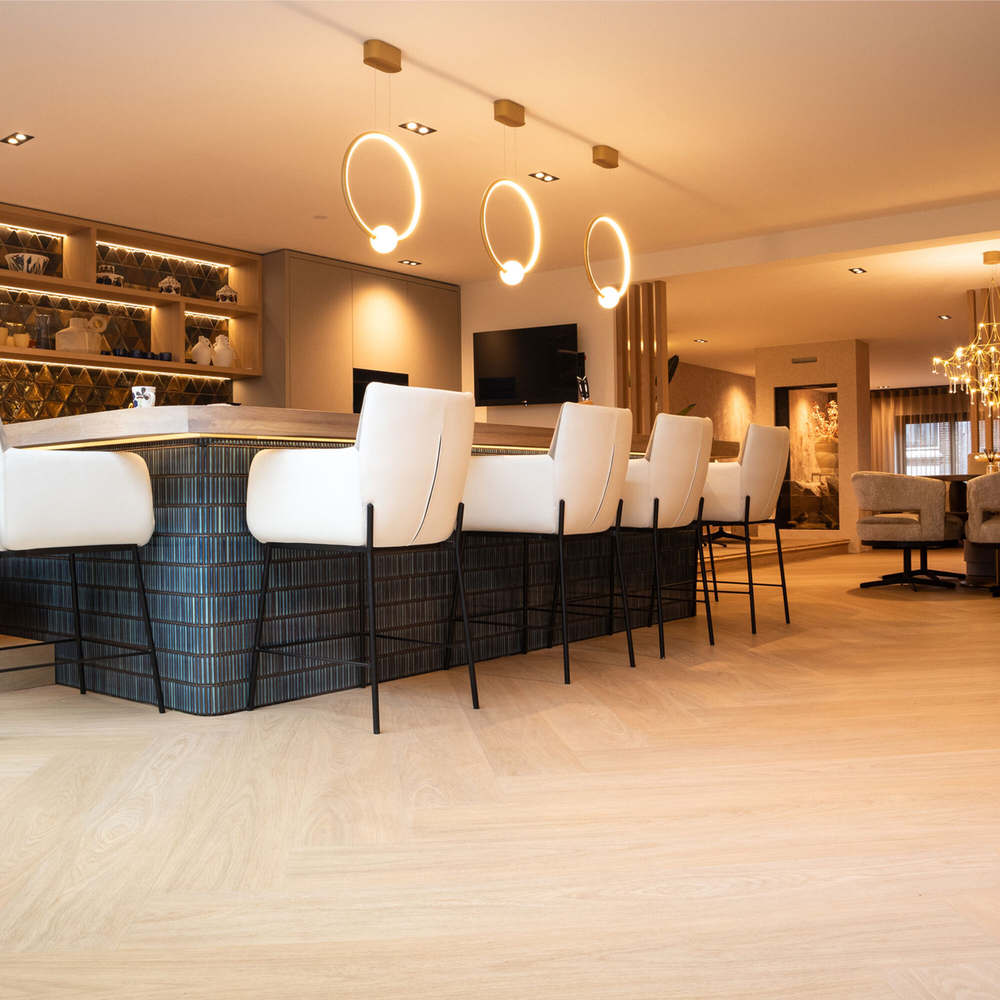 Lichte visgraat PVC-vloer in een luxe woonkeuken met een groot kookeiland, witte barkrukken en moderne ringvormige hanglampen.