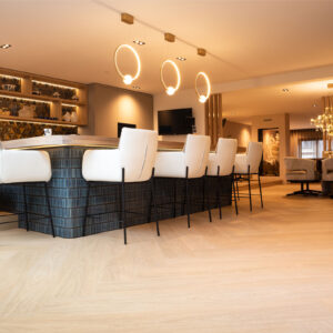 Lichte visgraat PVC-vloer in een luxe woonkeuken met een groot kookeiland, witte barkrukken en moderne ringvormige hanglampen.