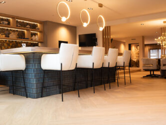 Lichte visgraat PVC-vloer in een luxe woonkeuken met een groot kookeiland, witte barkrukken en moderne ringvormige hanglampen.