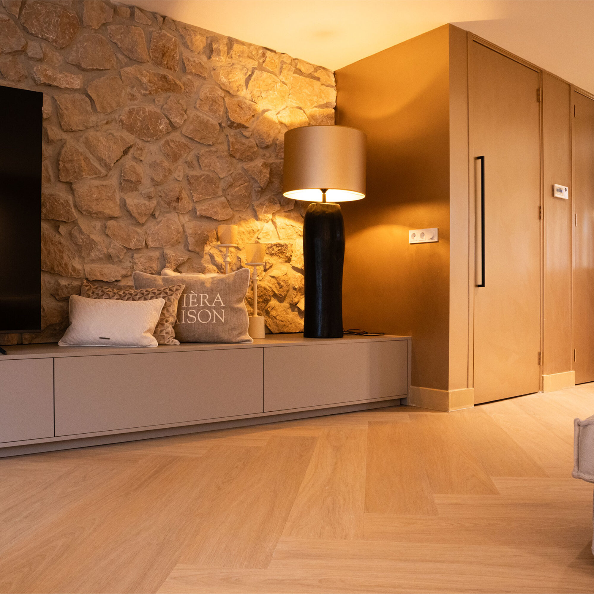 Lichte eiken PVC-vloer in een moderne woonkamer met een stenen muur, stijlvolle verlichting en een warme sfeer.
