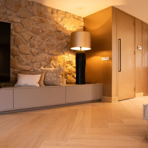 Lichte eiken PVC-vloer in een moderne woonkamer met een stenen muur, stijlvolle verlichting en een warme sfeer.