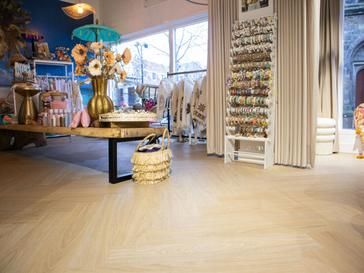 Lichte eiken PVC-vloer in een winkelruimte met kleurrijke inrichting, een tafel en rekken met producten.