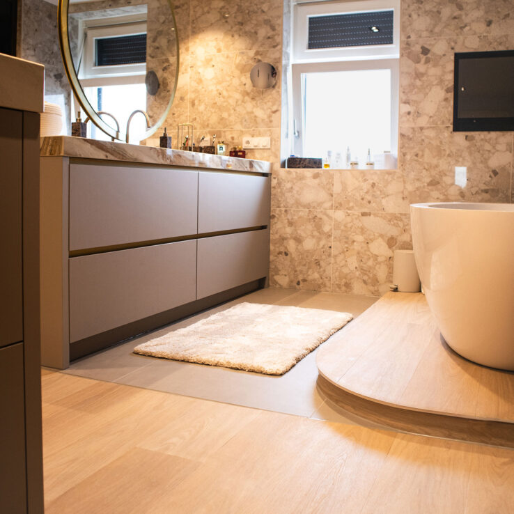 Moderne badkamer met vrijstaand bad, terrazzo wandtegels en een lichte houtlook PVC-vloer voor een warme, luxe uitstraling.