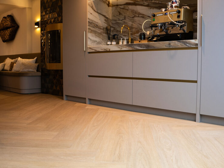 Lichte eiken Dinograatvloer in een luxe keuken met marmeren achterwand, ingebouwde koffiecorner en warme indirecte verlichting.
