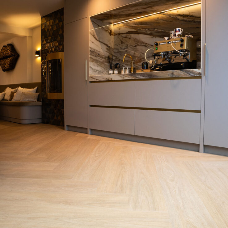 Lichte eiken Dinograatvloer in een luxe keuken met marmeren achterwand, ingebouwde koffiecorner en warme indirecte verlichting.