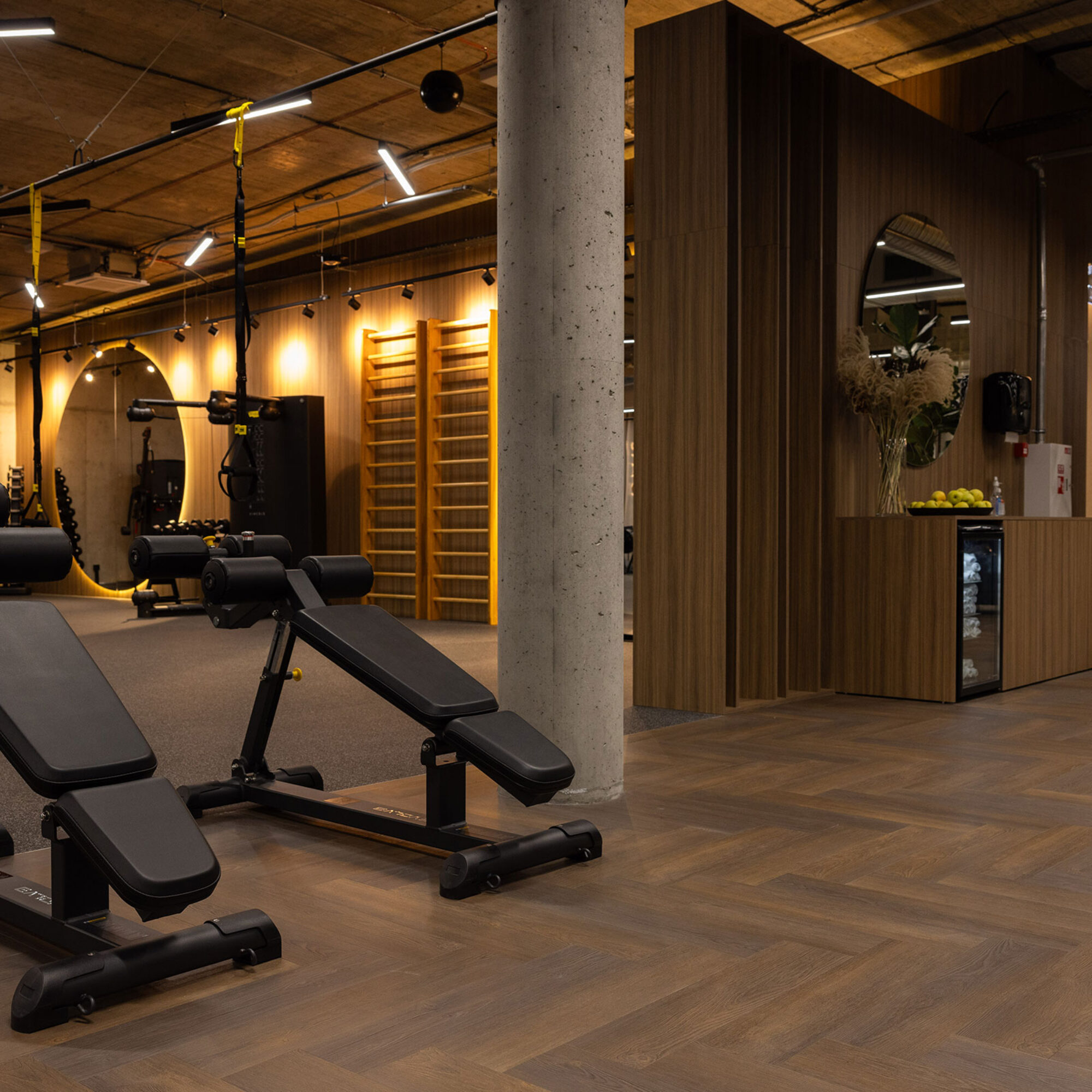 Donkere eiken visgraatvloer in een luxe fitnessruimte met houten wanden, moderne apparatuur en warme verlichting.