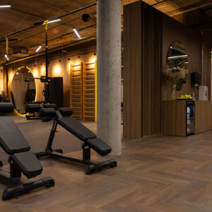 Donkere eiken visgraatvloer in een luxe fitnessruimte met houten wanden, moderne apparatuur en warme verlichting.
