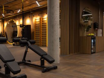 Donkere eiken visgraatvloer in een luxe fitnessruimte met houten wanden, moderne apparatuur en warme verlichting.
