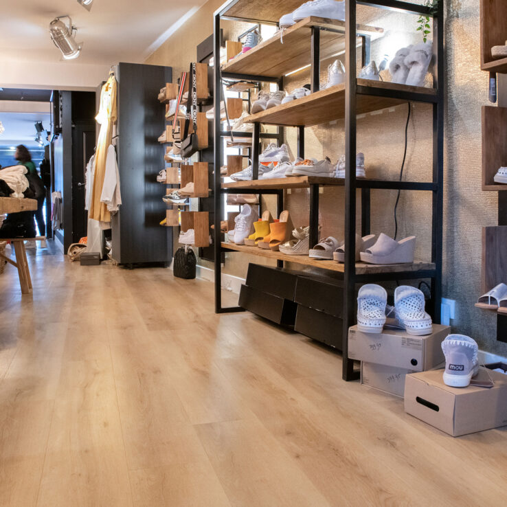 Lichte eiken PVC-vloer in een moderne schoenen- en kledingwinkel met open schappen, warme verlichting en een natuurlijke uitstraling.
