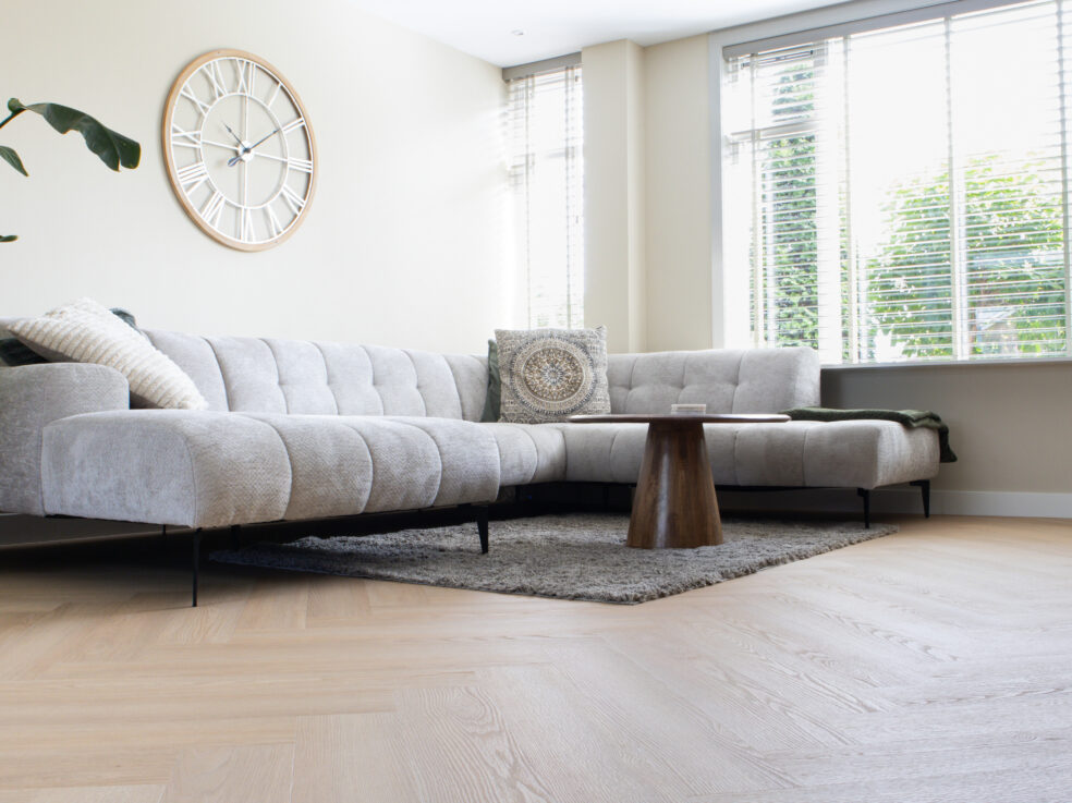 Lichte eiken PVC-vloer in een moderne woonkamer met een comfortabele bank en veel natuurlijk licht.