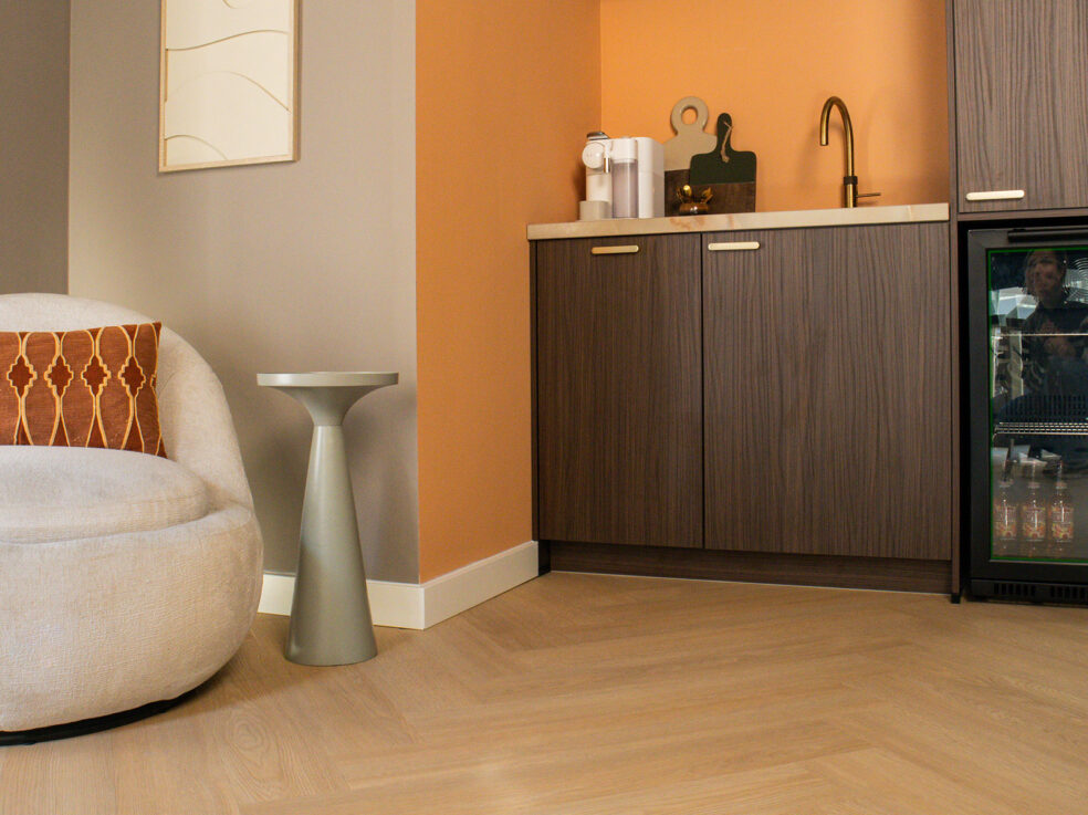 Lichte eiken PVC-vloer in een gezellige woonkamer met een zithoek, een moderne kast en een kleurrijke muur.