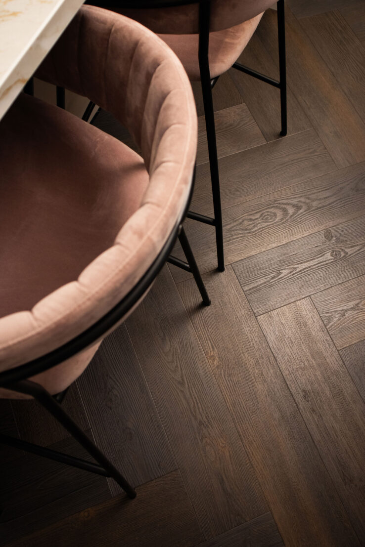 Donkere visgraat PVC-vloer met zicht op roze fluwelen eetkamerstoelen met zwarte poten en een marmerlook tafelblad.