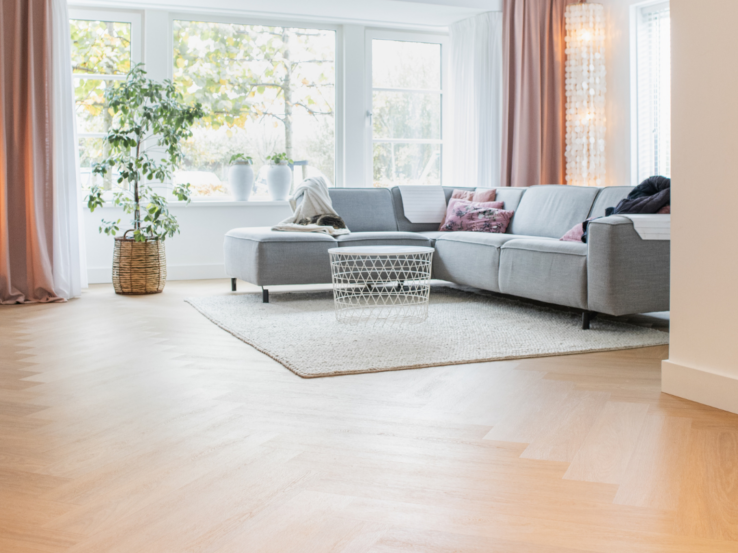 Lichte eiken PVC-vloer in een moderne woonkamer met een comfortabele bank, grote ramen en veel natuurlijk licht