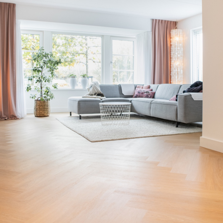 Lichte eiken PVC-vloer in een moderne woonkamer met een comfortabele bank, grote ramen en veel natuurlijk licht