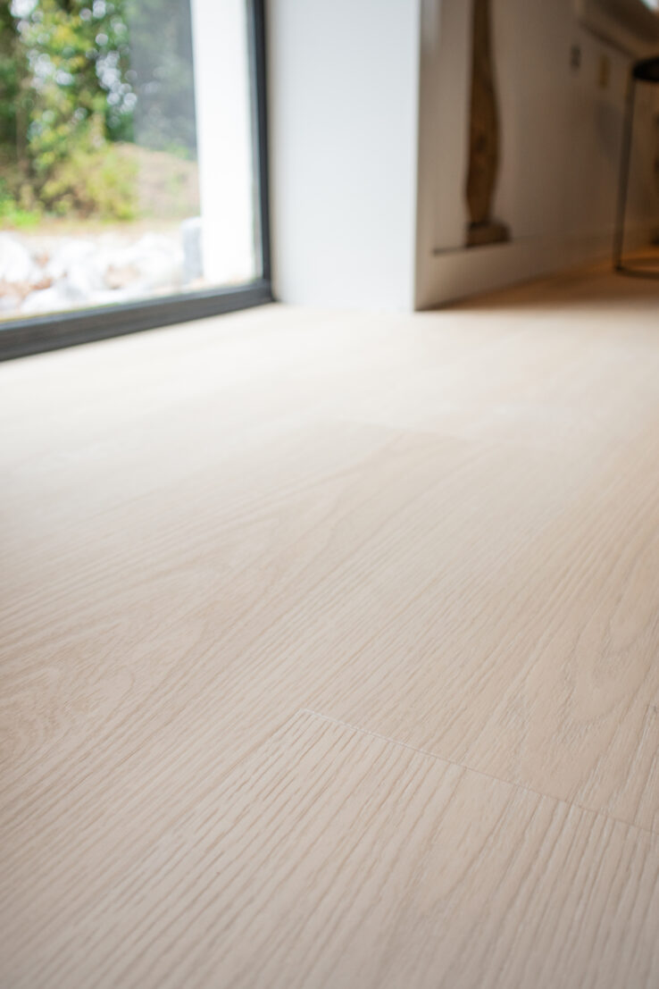 Close-up van een heel lichte eiken PVC-vloer met zachte houtnerf en een rustige, egale uitstraling.