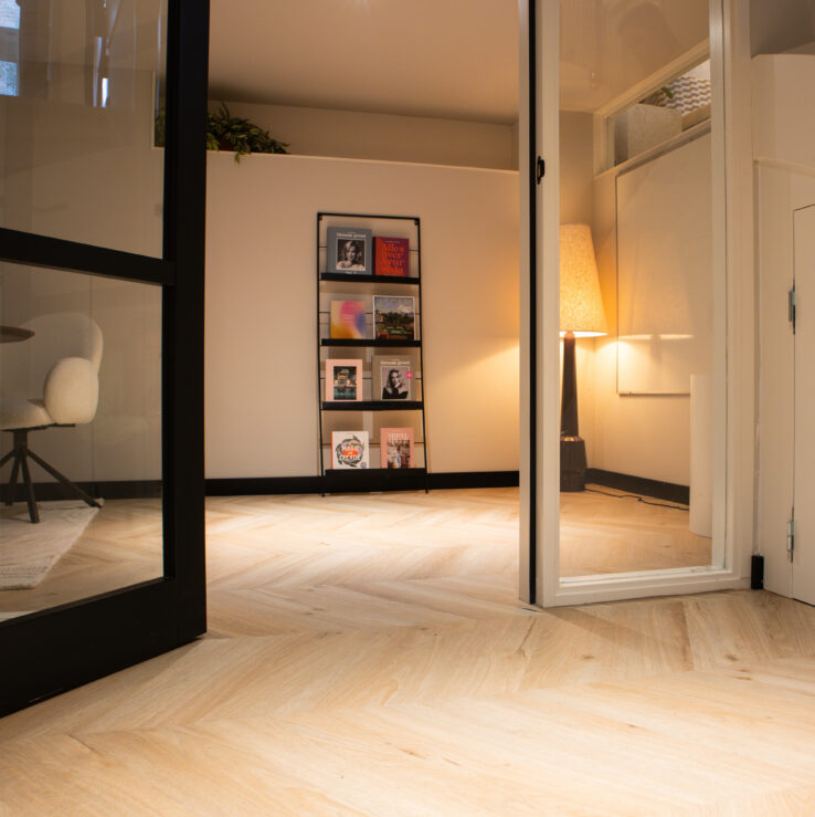 Lichte eiken PVC-vloer in een moderne ruimte met een glazen wand, een boekenplank en een stijlvolle bureaustoel.