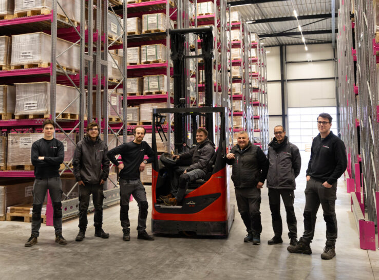 Een afbeelding met zeven mannen die op een rijtje in het magazijn van Vivafloors staan