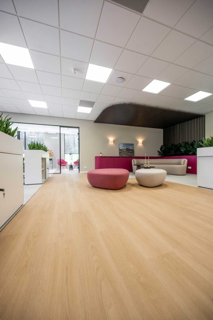 Lange kantoorruimte met lichte houten vloer en een lounge met roze poefs in het Vivafloors pand