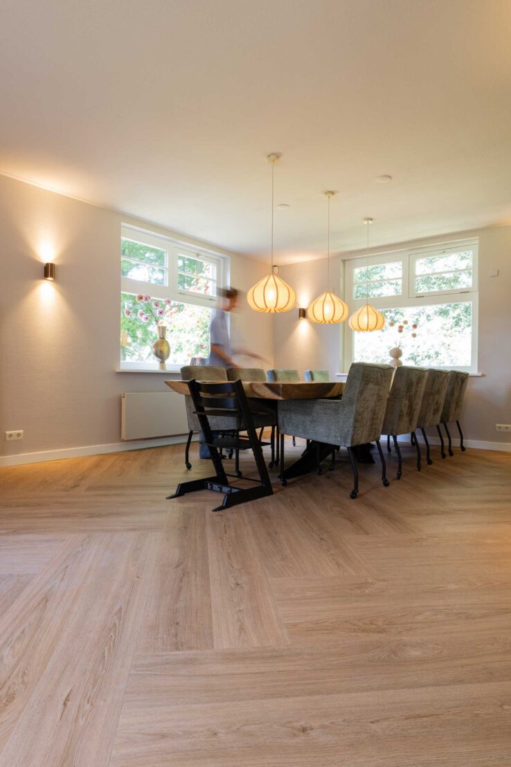 Eetkamer met lange tafel en hanglampen op houten visgraatvloer in Haaksbergen