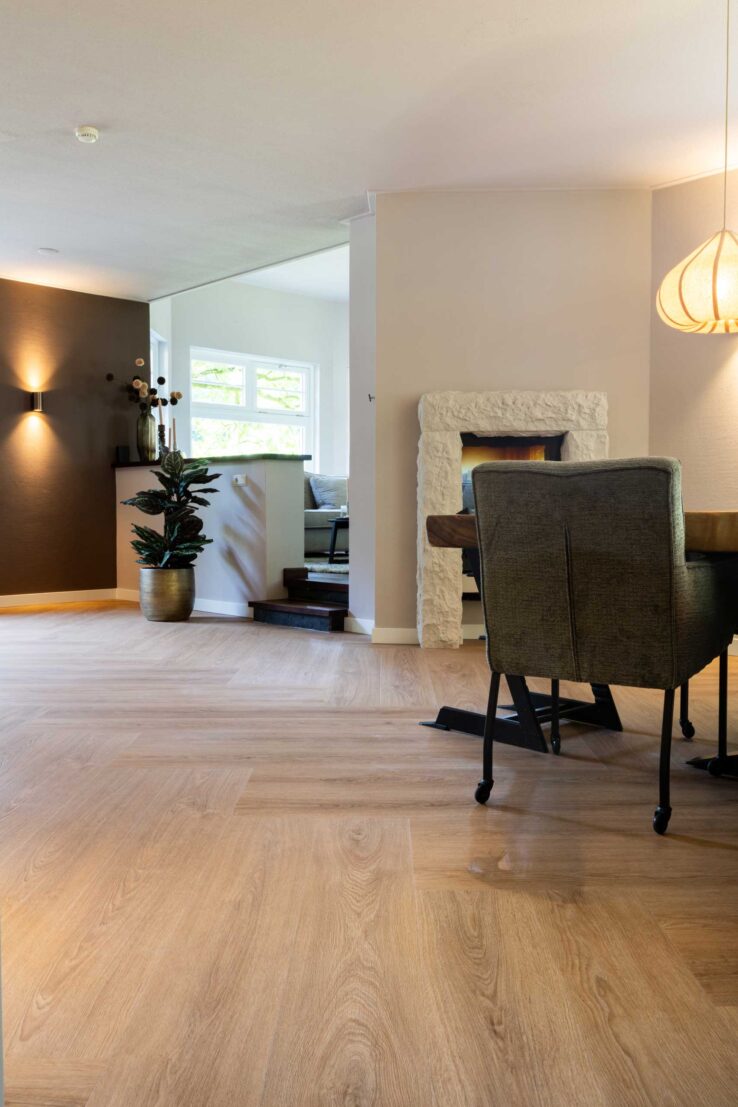 Doorkijk naar woonkamer met open haard en houten visgraatvloer in Haaksbergen