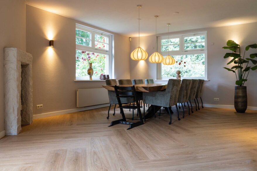 Eetkamer met lange tafel, hanglampen en houten visgraatvloer in een woning in Haaksbergen