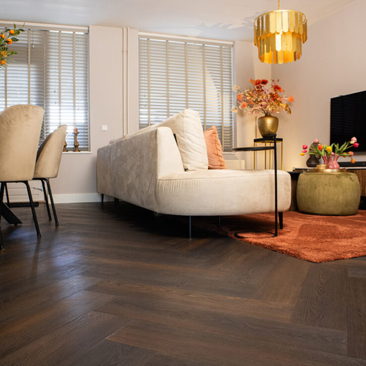 Woonkamer met witte bank, gouden hanglamp en oranje vloerkleed op donkere vloer Visgraat 4540