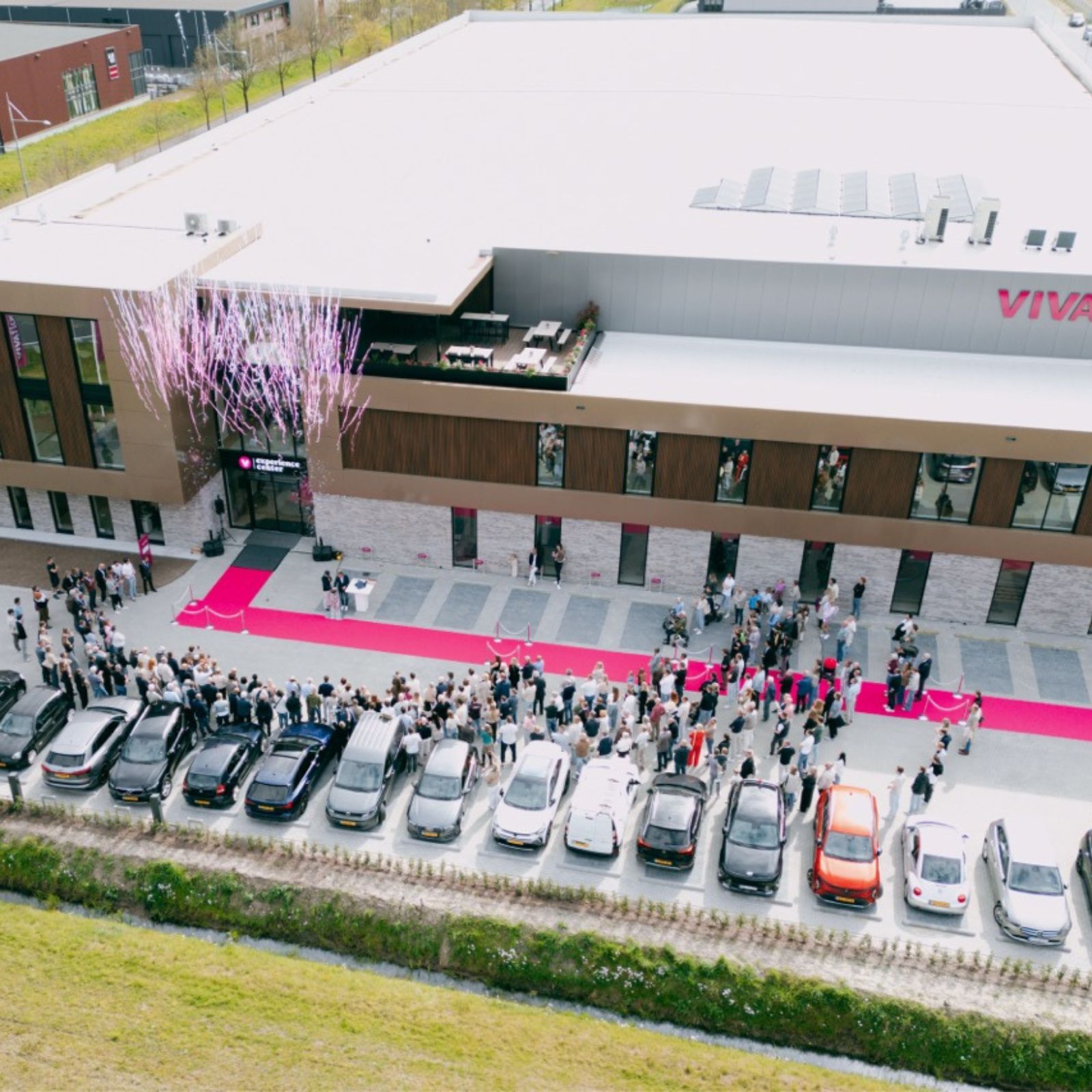 Luchtfoto van de opening van het nieuwe Vivafloors pand met roze loper, bezoekers en geparkeerde auto's